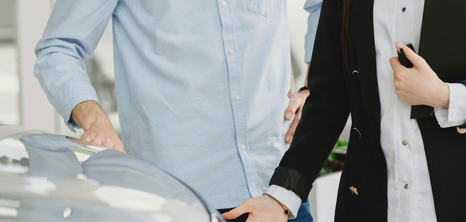homem vestido com camisa azul passa a mão no capô de um carro cinza